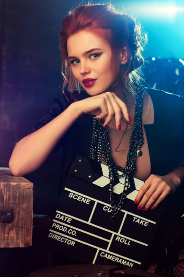 Red haired woman in black shirt and matching jewelry holding a film slate