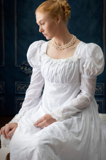 A red haired woman in a white regency style dress and filigree collar necklace