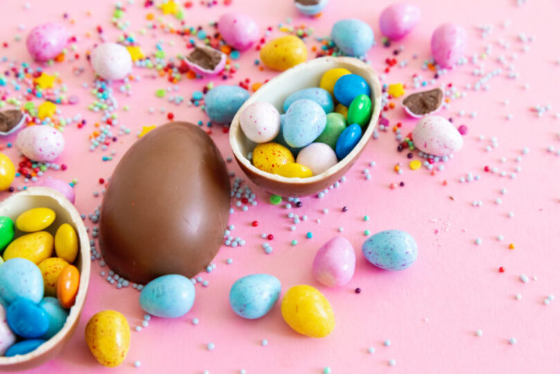 Assorted Easter themed candies and chocolate eggs on pink background