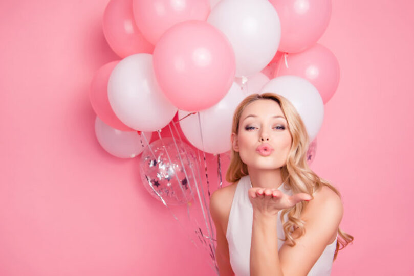 Blonde woman with pink and white balloons blowing a kiss