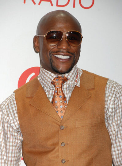 Floyd Mayweather Jr. is wearing shades and a white striped dressy shirt. Brown tie and a brown vest.