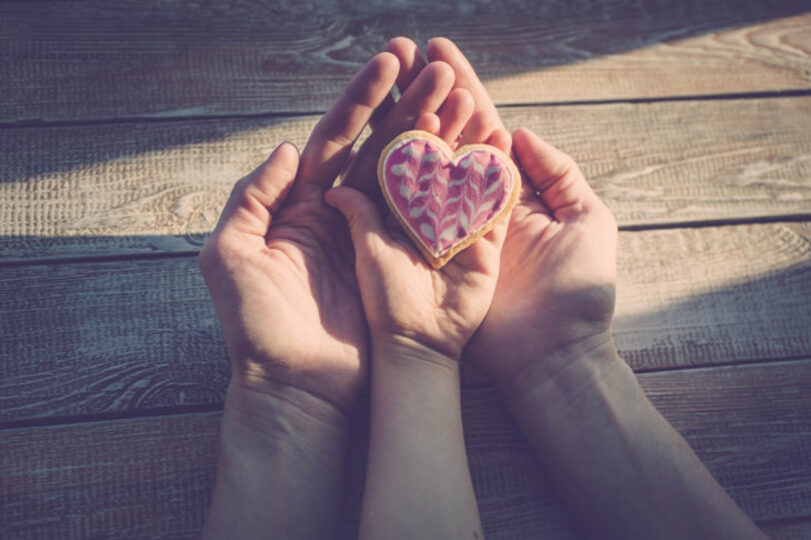 A heart shaped frosted cookie held in a mother and child's hand