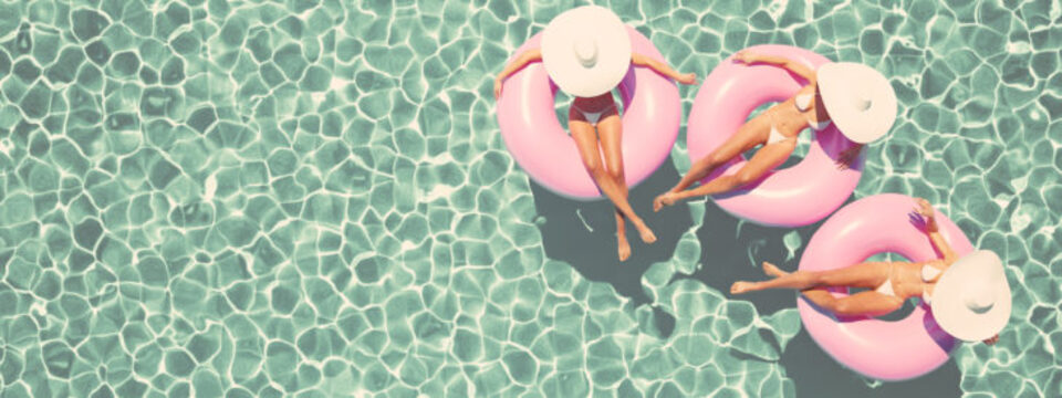 Three women in big hats and on floaties in a swimming pool