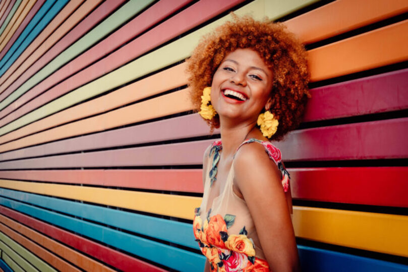 Beautiful black woman smiling posing in front of rainbow colored wall.