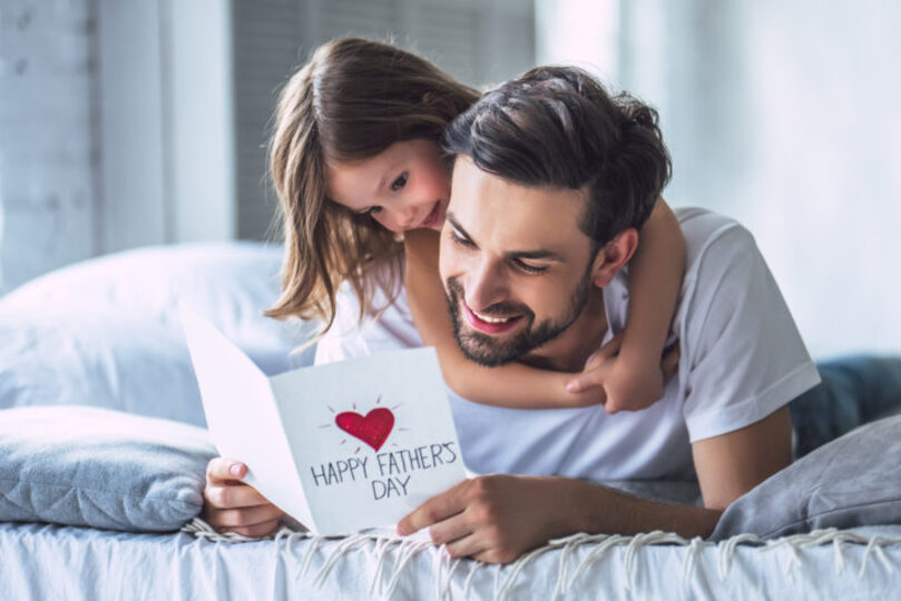 Daughter laying on and hugging dad while he reads a fathers day card
