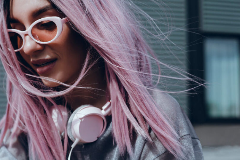 young girl with light pink hair and sunglasses, headphone around her neck walking around