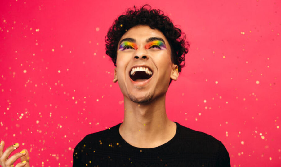 Excited gay man with rainbow makeup and glitter flying
