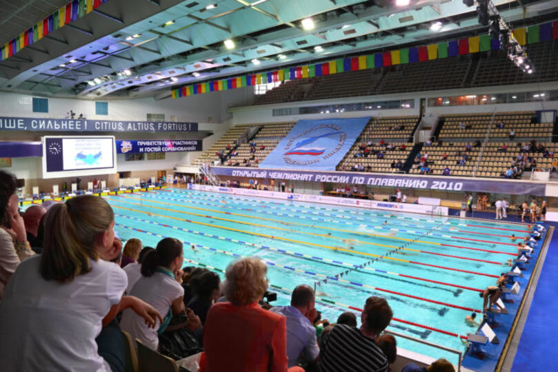 People sitting in the stands of a stadium with an Olympic swimming pool