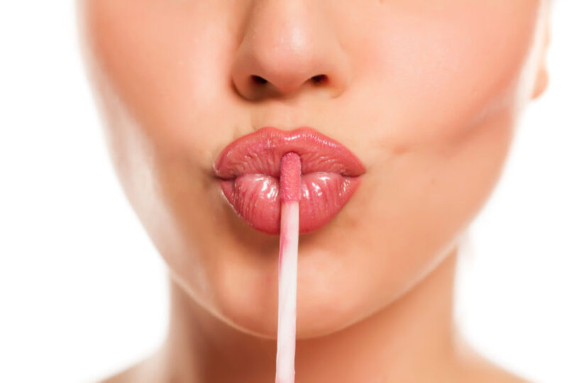 Young woman putting on lip gloss, just nose and mouth in frame and she is holding the stick to her lips in duck face