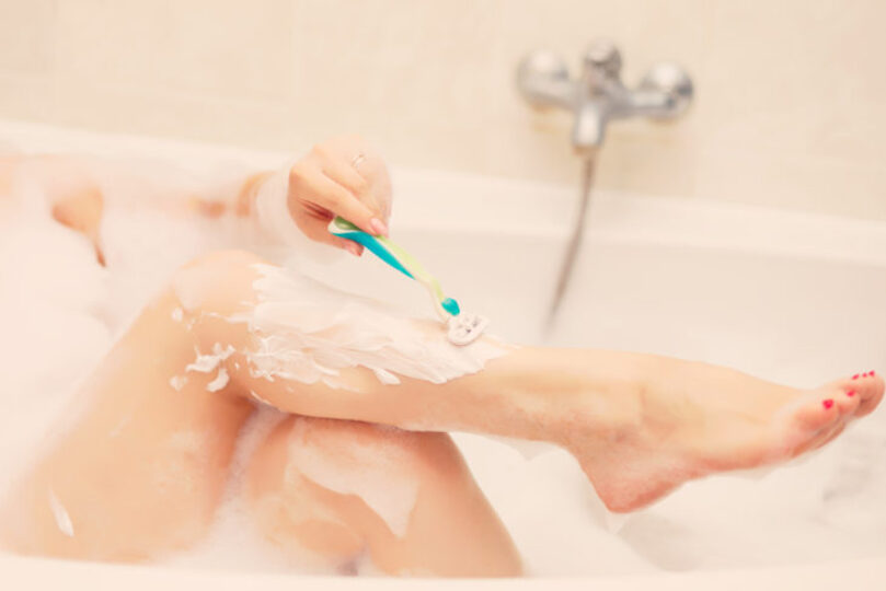 woman shaving her legs in the bathtub