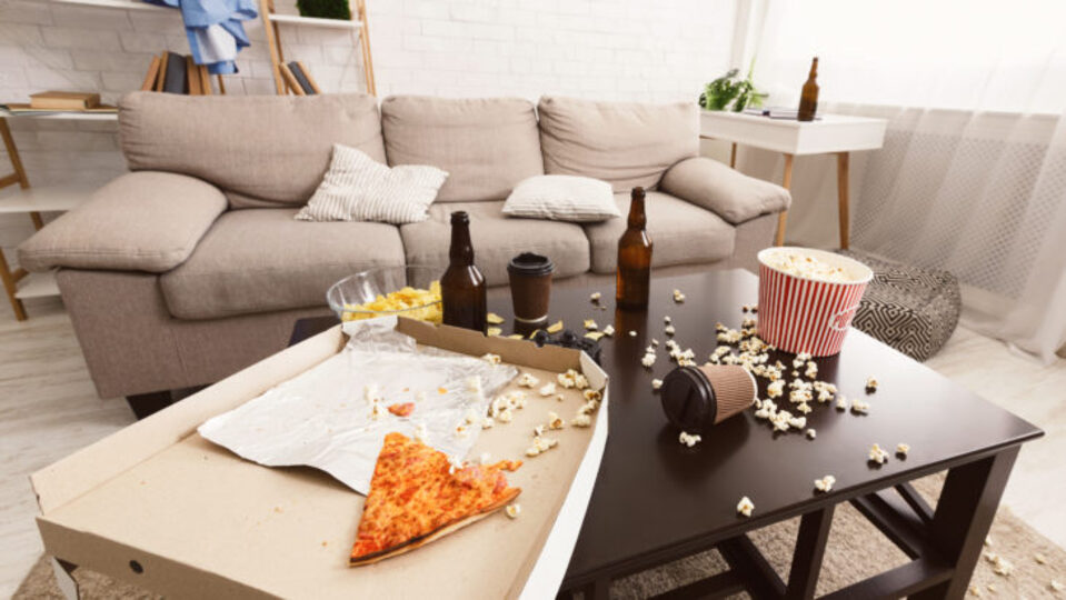 messy college apartment coffee table with beer bottles, popcorn, and pizza all over the table