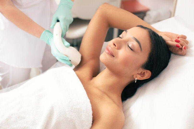 Beautiful woman lying on a table with her arm up getting laser hair removal done on her armpits