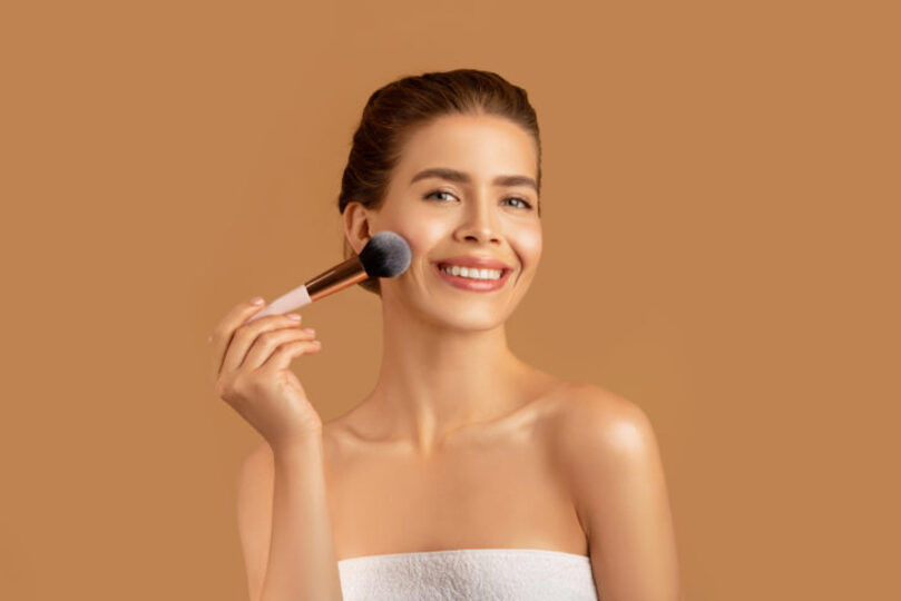 young woman in a towel putting on soft glam makeup, still looks natural but elevated