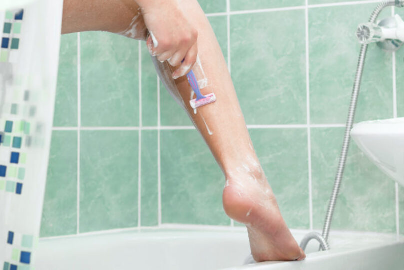 woman standing in the shower with one leg up on bathtub shaving it