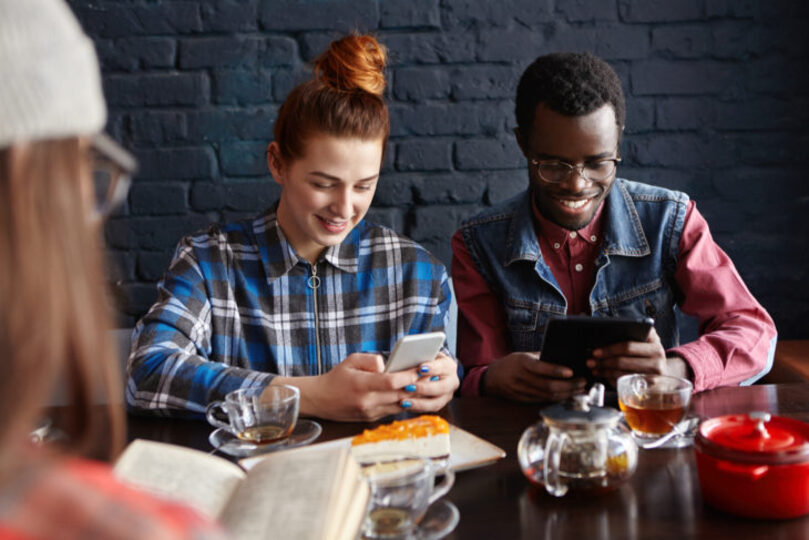 Two friends using and smiling at their phones