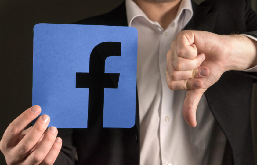 Someone holding a Facebook sign and making a thumbs-down 
