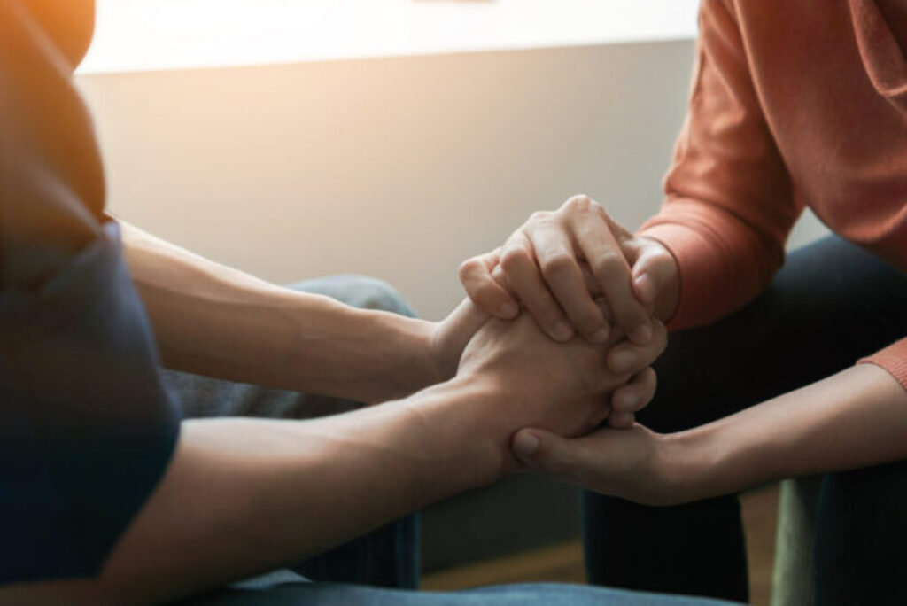 Two people holding hands to console/support them through therapy/talking
